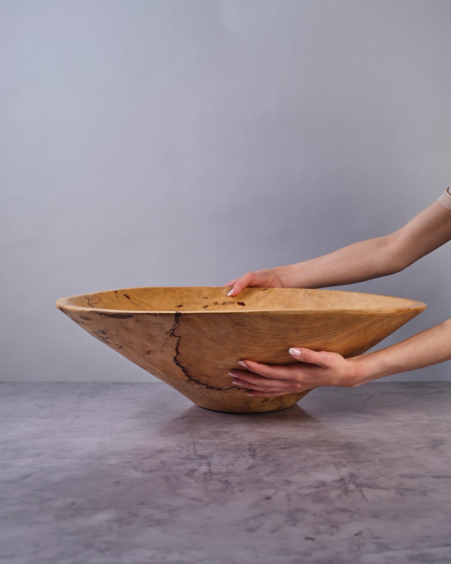Wooden bowl held by a hand on a gray background