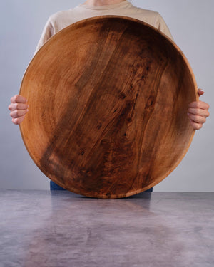 Person holding a large wooden bowl against a plain background
