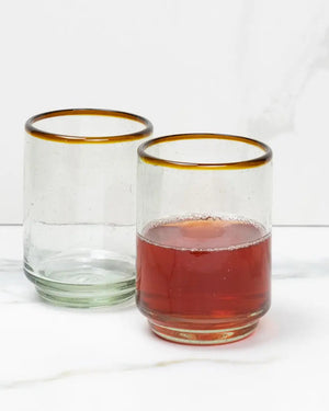 Two glass tumblers with gold rims, one filled with a red liquid on a white background