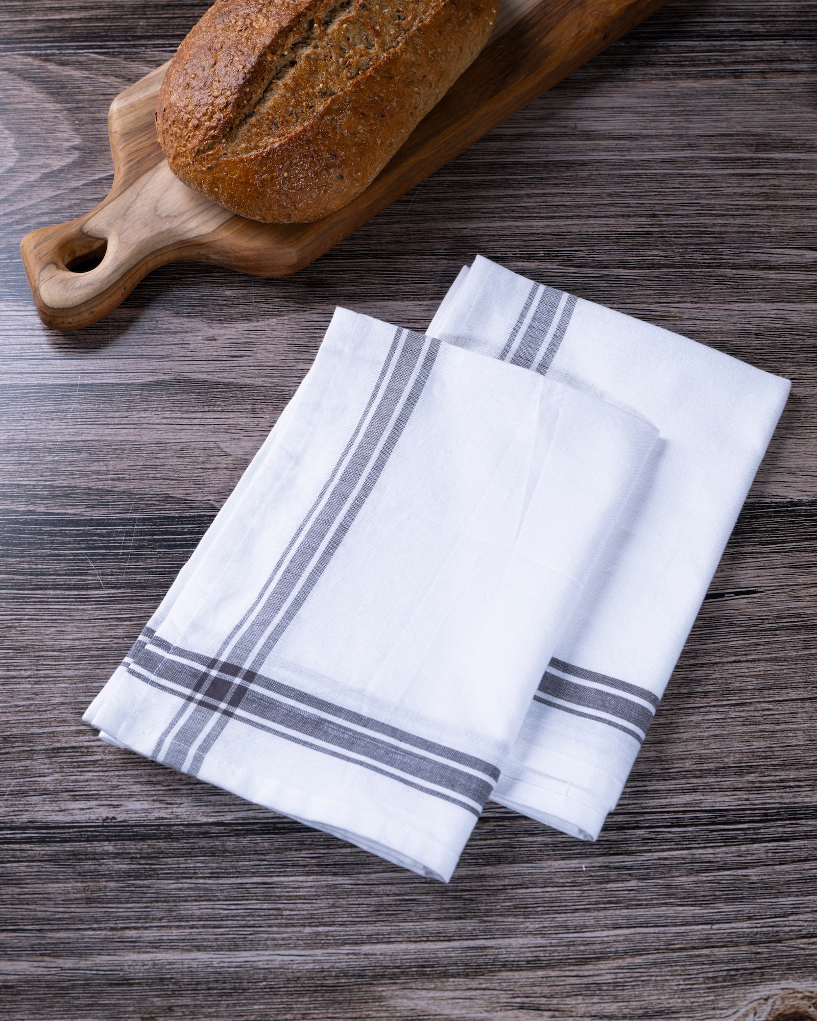 White kitchen towels with gray stripes on a wooden surface with bread.