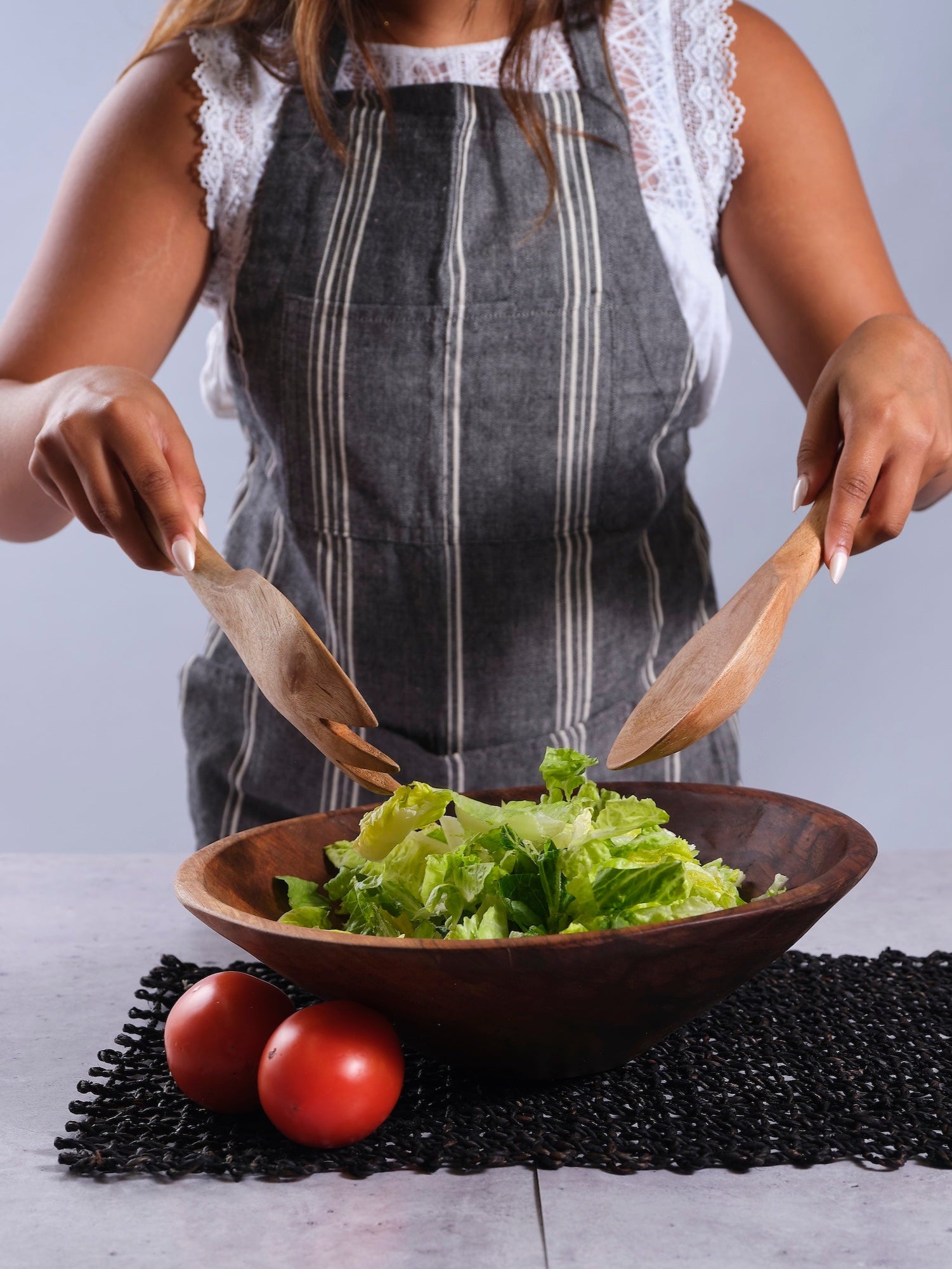 Person preparing a salad with wooden utensils in TerraKlay's 14 inch classic round wooden bowl.
