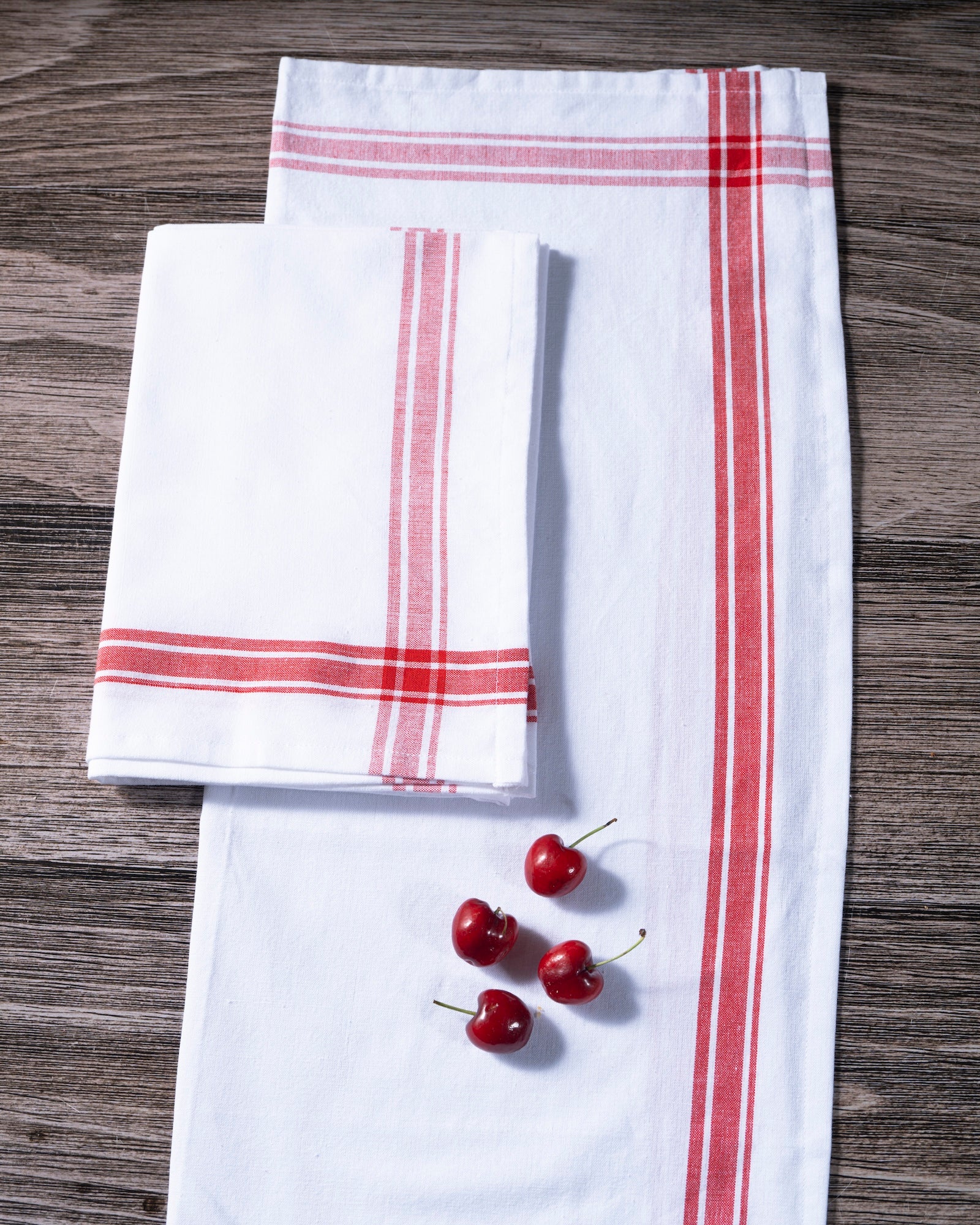 White kitchen towels with red stripes on a wooden surface with cherries.