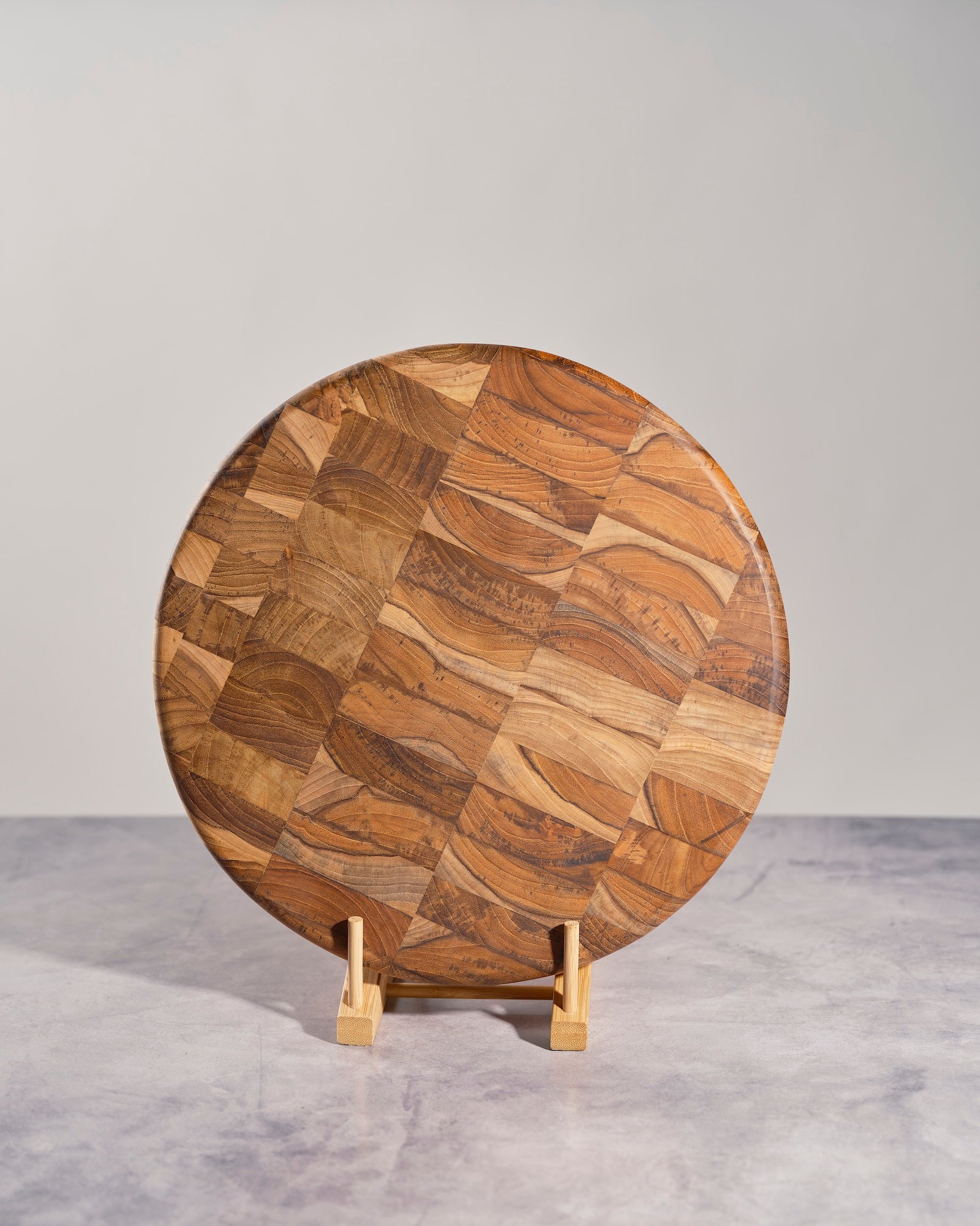 Round wooden cutting board with a pattern on a stand against a gray background