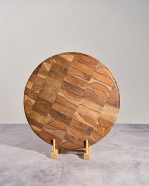 Round wooden cutting board with a pattern on a stand against a gray background