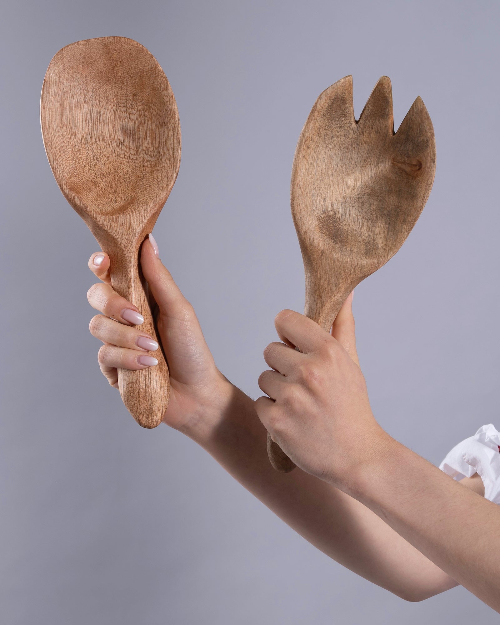 Wooden spoon and fork held by a person against a gray background