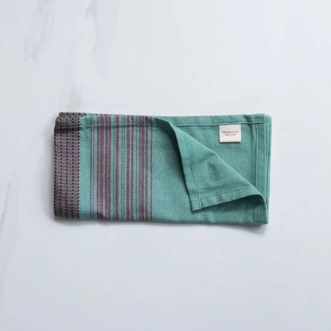 Folded large teal cotton napkins with brown stripes from TerraKlay on a marble surface.
