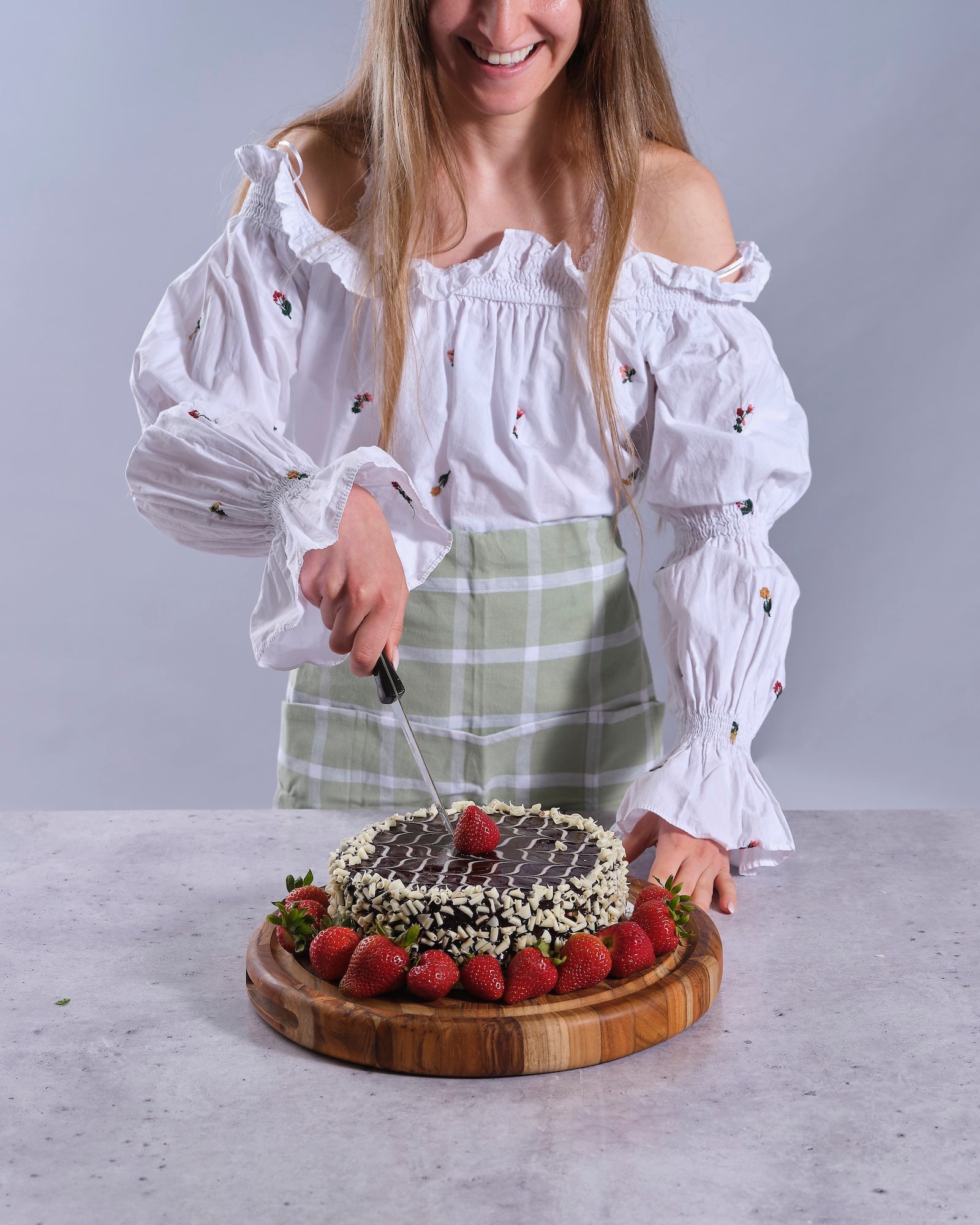 Woman cutting a decorated cake with strawberries on a TerraKlay's wooden board.